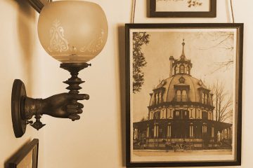 A wall lamp shaped like a hand next to an old framed photograph of The Octagon House