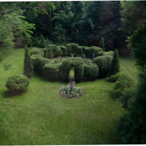 Circular hedge maze with central flower bed on a grassy lawn.