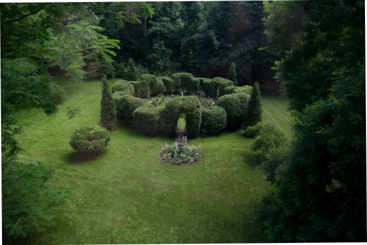Circular hedge maze with central flower bed on a grassy lawn.