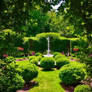 Garden with central statue, surrounded by green bushes and trees.