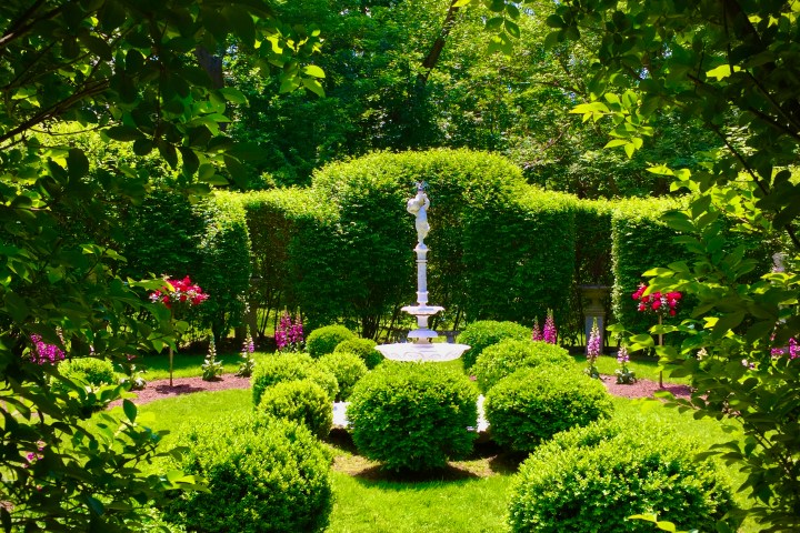 Garden with central statue, surrounded by green bushes and trees.
