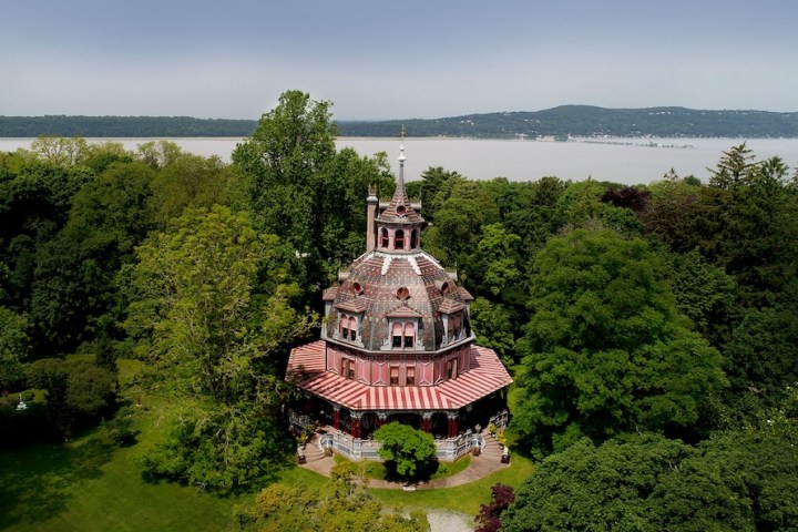 Octagonal Victorian house surrounded by trees, overlooking a large body of water.