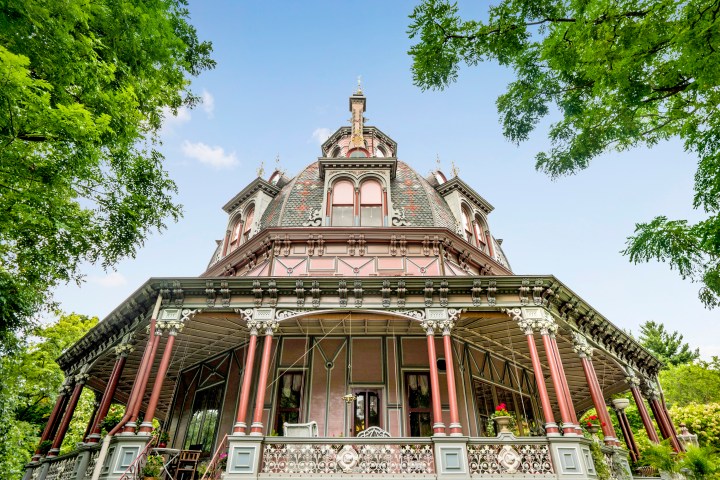 Victorian-style octagonal house with ornate details and surrounding trees.