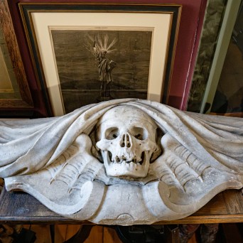 Stone skull sculpture with draped fabric on a shelf, framed art in background.